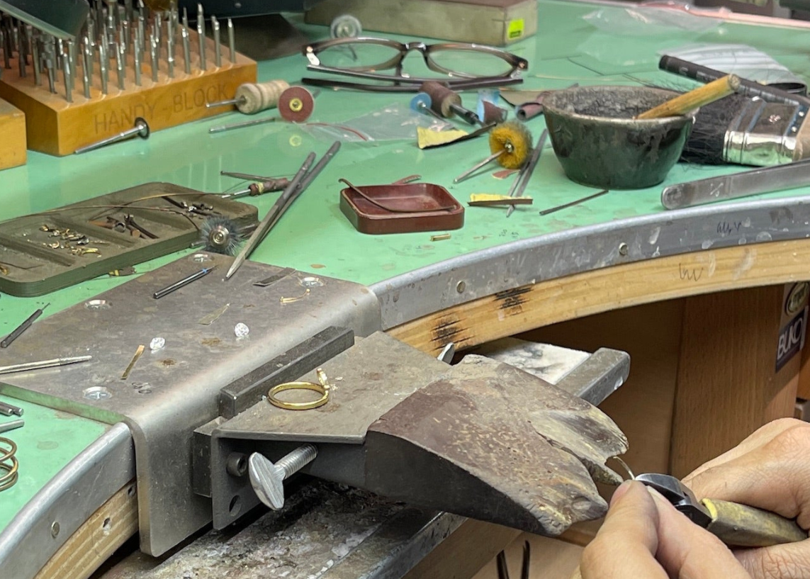 Workbench with jewelry-making tools and materials, including a ring being worked on.