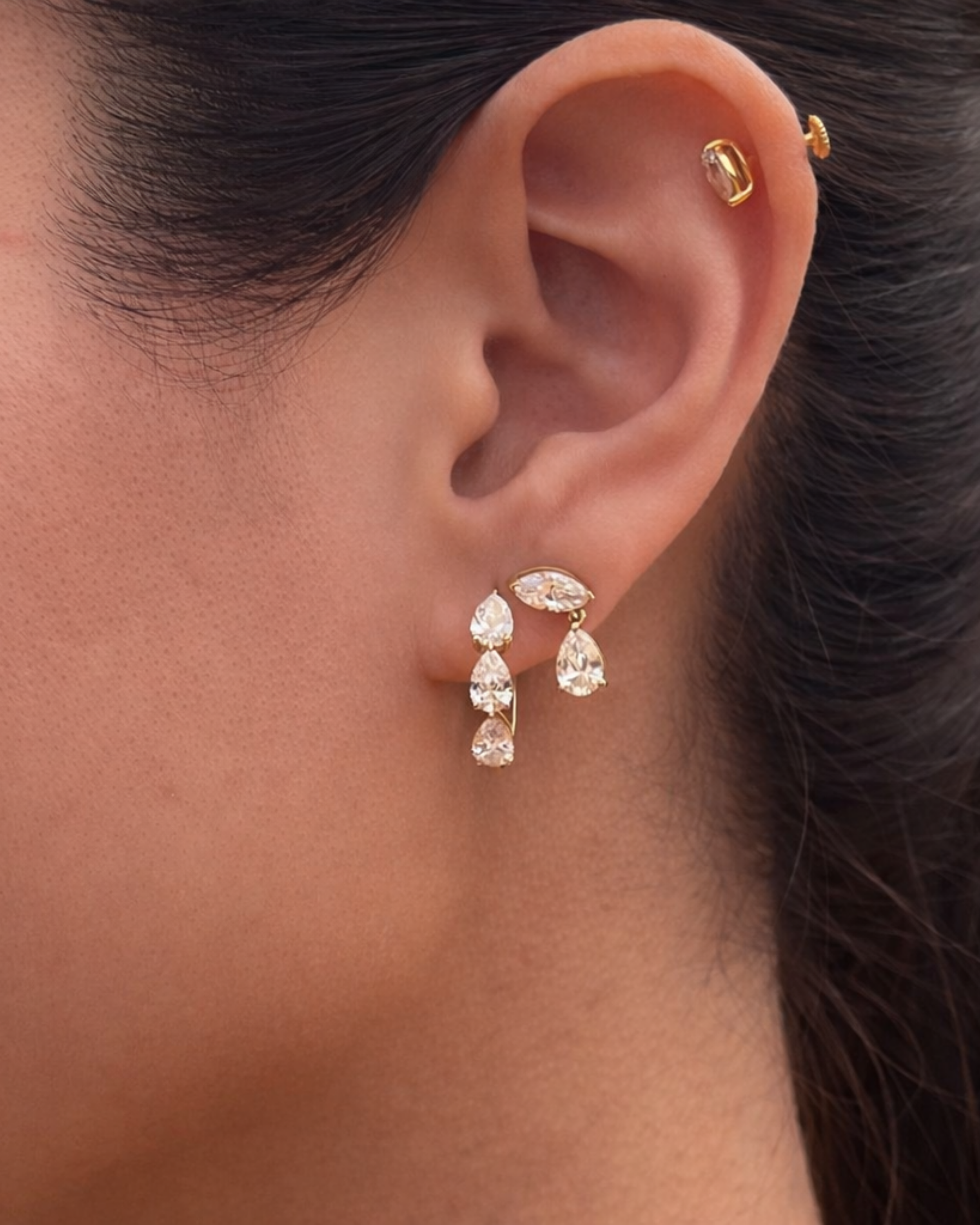 Close-up of an ear wearing gold earrings with clear gemstones.