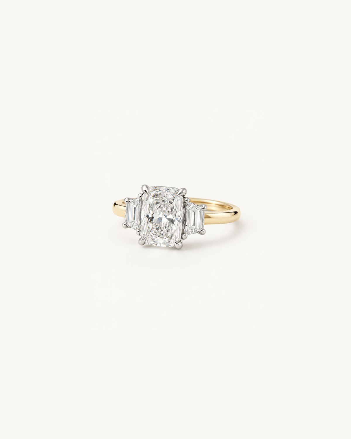 A three-stone diamond ring featuring a large cushion-cut center diamond flanked by two smaller baguette diamonds, set in a yellow gold band with silver-colored prongs, on a clean white background.